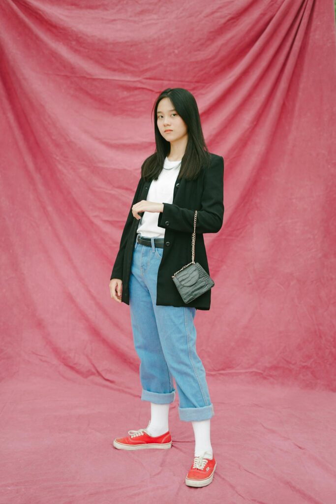 A fashionable woman poses confidently against a pink background, showcasing modern style.