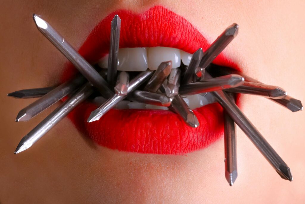 Artistic close-up of red lips biting metal spikes, contrasting beauty and strength.